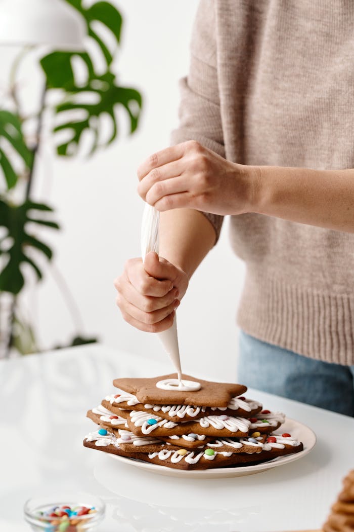 Close-up of hands icing a stack of homemade Christmas cookies.
